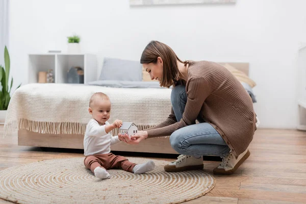 Positive parent holding toy house near son on rug in bedroom — Stock Photo