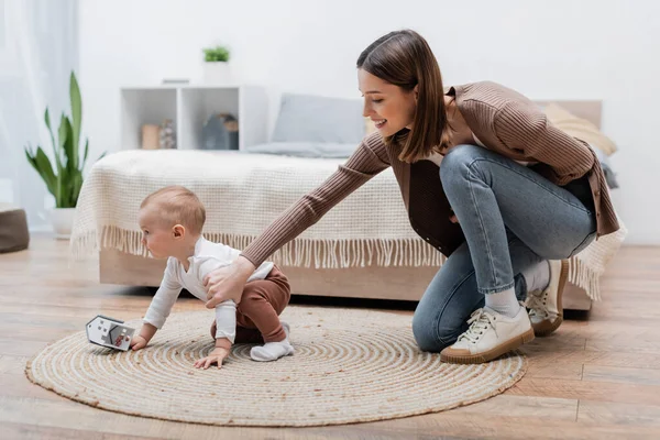 Smiling mom touching baby boy with toy house in bedroom — Stock Photo