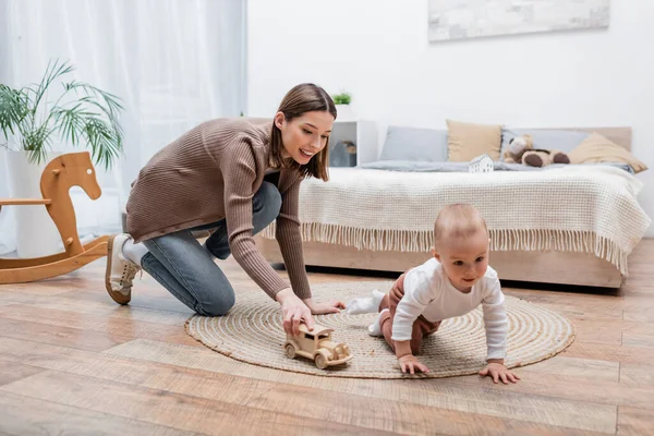 Happy young woman playing with toy car near baby son at home — Stock Photo