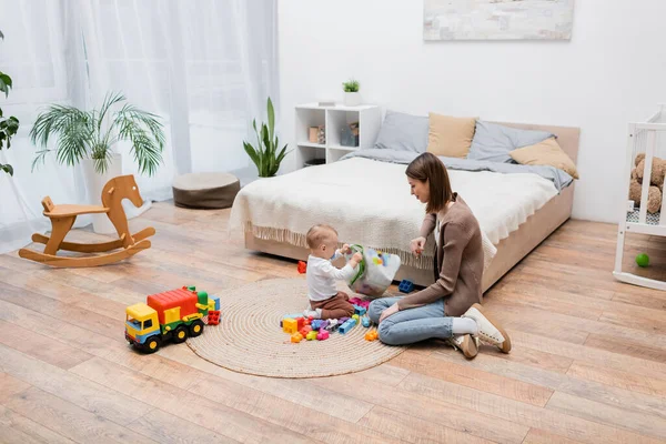 Parent sitting near baby son holding bag and building blocks at home — Stock Photo