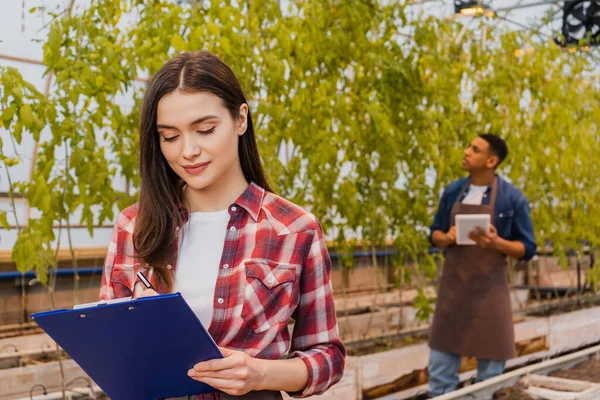 Young farmer writing on clipboard in greenhouse — Stock Photo