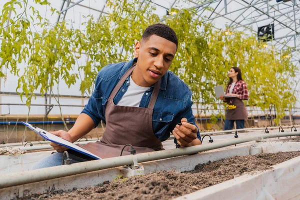 Agricoltore afroamericano che tiene appunti vicino al terreno negli appunti — Foto stock