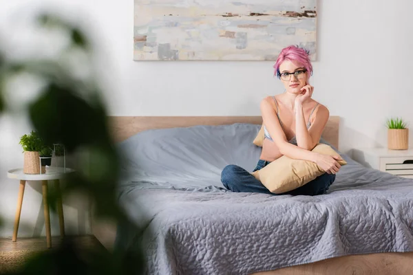 Jovem com cabelo tingido sentado em sutiã de seda e jeans na cama — Fotografia de Stock