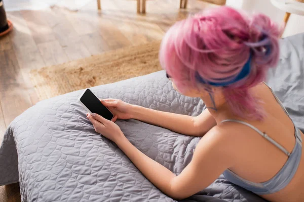 Vista de ángulo alto de la mujer joven con el pelo teñido acostado en la cama mientras chatea en el teléfono inteligente — Stock Photo