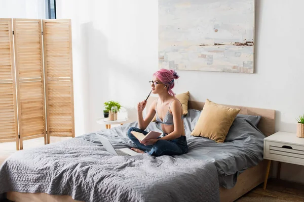 Pensive young woman with dyed hair holding notebook while studying online at home — Stock Photo