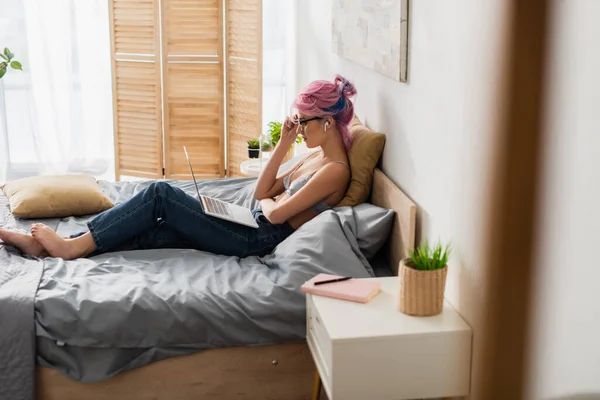 Vista lateral de la mujer descalza con el pelo teñido y auriculares ver la película en el ordenador portátil - foto de stock