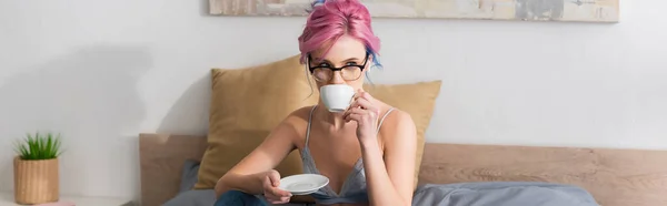 Молода жінка з рожевим волоссям і навушниками п'є каву, банер — стокове фото