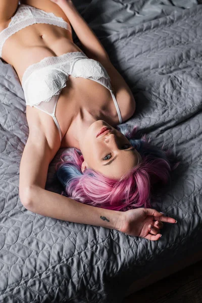 Вид сверху на татуированную и сексуальную молодую женщину в белых трусах лежащую на кровати — стоковое фото