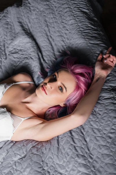 Top view of tattooed and sexy young woman in white bra lying on bed — Stock Photo