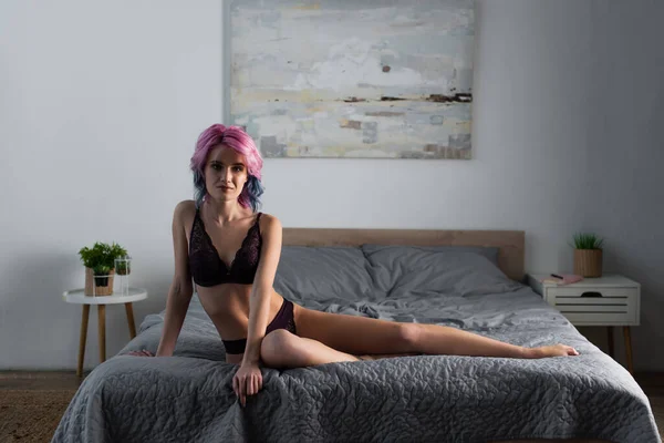 Mujer sexy con el pelo teñido en ropa interior de encaje oscuro posando en la cama - foto de stock