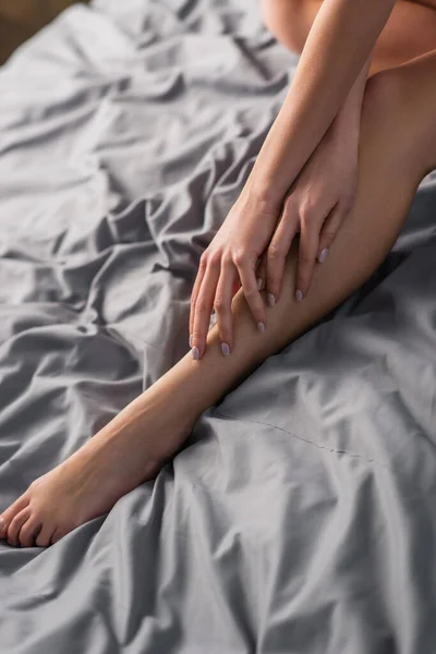 Vue recadrée de jeune femme sensuelle touchant la jambe sur le lit — Photo de stock