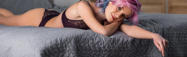 Mujer joven en ropa interior sexy oscura mirando a la cámara y acostado en la cama, pancarta - foto de stock