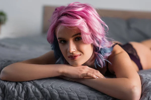 Retrato de jovem mulher com cabelo rosa olhando para a câmera e deitado na cama — Fotografia de Stock