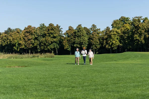 Interracial senior men walking with golf clubs on field — стоковое фото