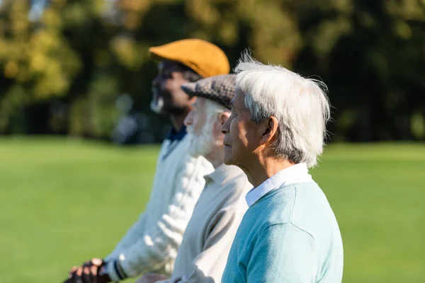 Vista lateral de asiático senior hombre cerca interracial amigos - foto de stock