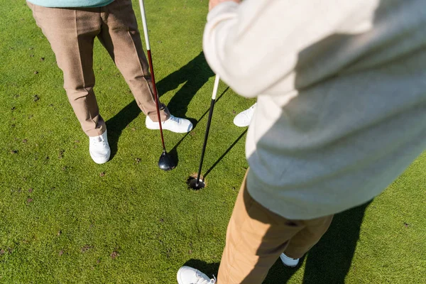 Vista cortada do homem sênior segurando bandeira vara perto de amigo no campo de golfe — Fotografia de Stock