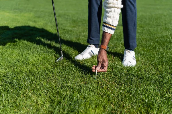 Обрізаний вид на афроамериканського старшого чоловіка, який розміщує трійник для гольфу на зеленому газоні — стокове фото