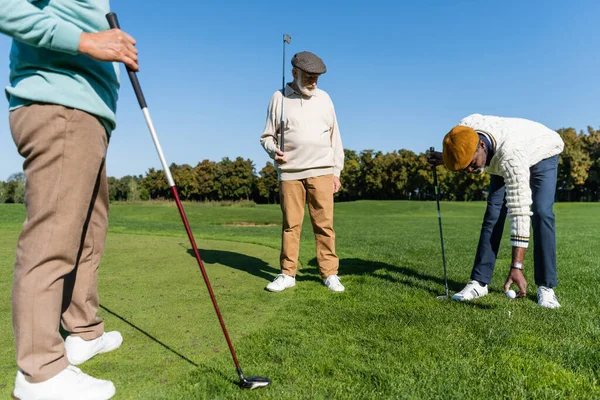 Afrikanisch-amerikanischer Senior platziert Ball auf Golfabschlag in der Nähe multiethnischer Freunde — Stockfoto
