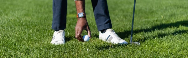 Cropped view of african american man placing ball on golf tee, banner — Stock Photo