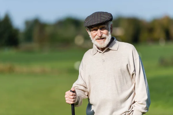 Wealthy senior man in flat cap standing with golf club — Stock Photo