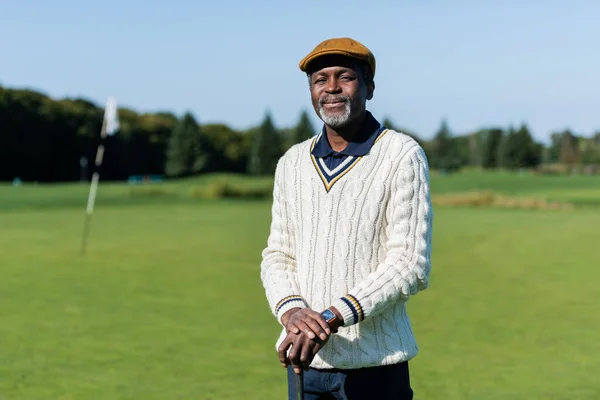 Cheerful african american man standing with golf club on green field — Stock Photo