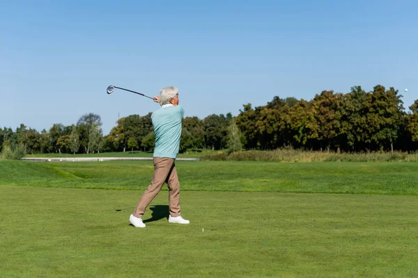 Longitud completa de asiático senior hombre jugando golf en verde césped - foto de stock