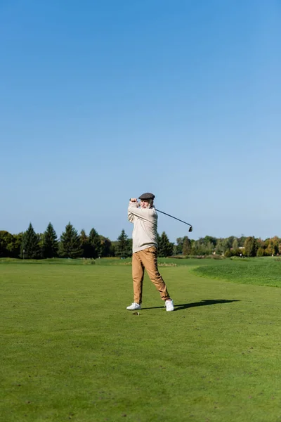 Comprimento total do homem sênior em cap plana jogando golfe no gramado verde — Fotografia de Stock