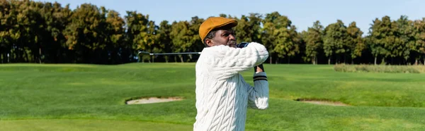 Hombre afroamericano de mediana edad en gorra plana jugando al golf, bandera - foto de stock