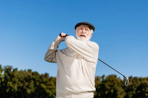 Bearded and senior man holding golf club while playing outdoors — стоковое фото