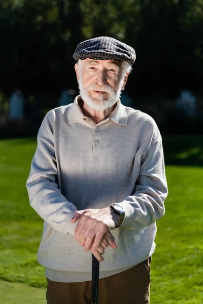 Bearded senior man in flat cap holding golf club — Stock Photo