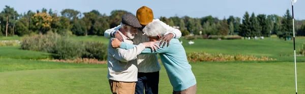 Senior interracial friends hugging near flag stick, banner — Stock Photo
