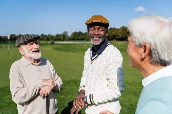 Happy and senior multiethnic men looking at blurred asian friend — стоковое фото