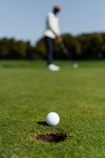 Pelota de golf en la hierba del campo verde cerca de golfista borrosa - foto de stock