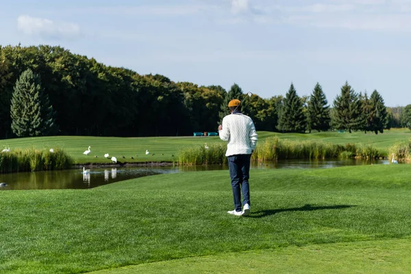 Back view of african american man holding golf club and walking on green field — Stock Photo