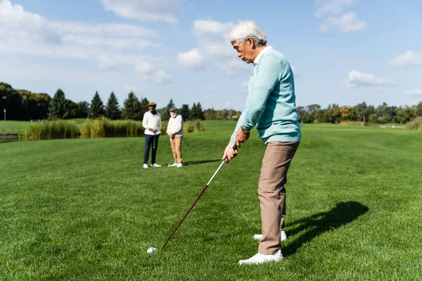 Senior asiático hombre jugando golf cerca amigos en borrosa fondo - foto de stock