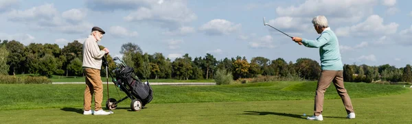 Старший азіатський чоловік грає в гольф біля друга з візком для гольфу, банер — стокове фото