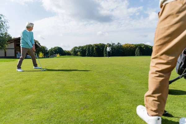 Старший азиатский мужчина играет в гольф с богатыми межрасовыми друзьями на лужайке — стоковое фото