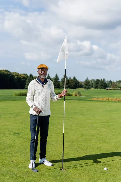 Rico africano americano senior hombre de pie con bandera palo y golf club - foto de stock