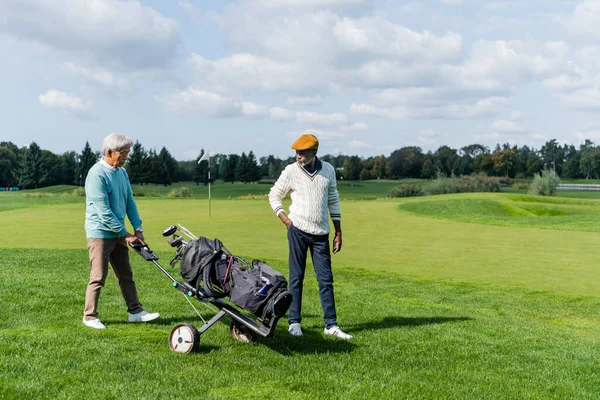 Asiatischer Senior läuft mit Golfwagen in der Nähe wohlhabender afrikanisch-amerikanischer Freund — Stockfoto