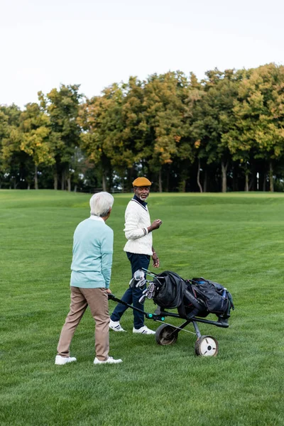 Homem americano africano sênior andando perto amigo com carrinho de golfe — Fotografia de Stock