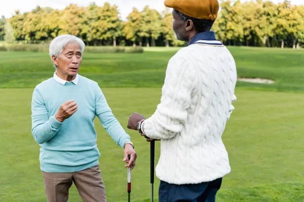 Старший азиатский мужчина разговаривает с африканским американским другом в плоской кепке — стоковое фото