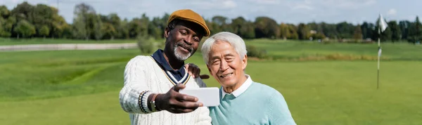 Africano americano hombre tomando selfie con senior feliz asiático amigo, bandera - foto de stock