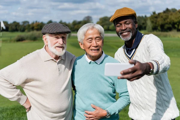 Веселий афроамериканський чоловік бере селфі з старшими міжрасовими друзями — стокове фото