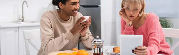 Щасливий афроамериканський чоловік дивиться на дівчину з цифровим планшетом під час сніданку, банер — стокове фото