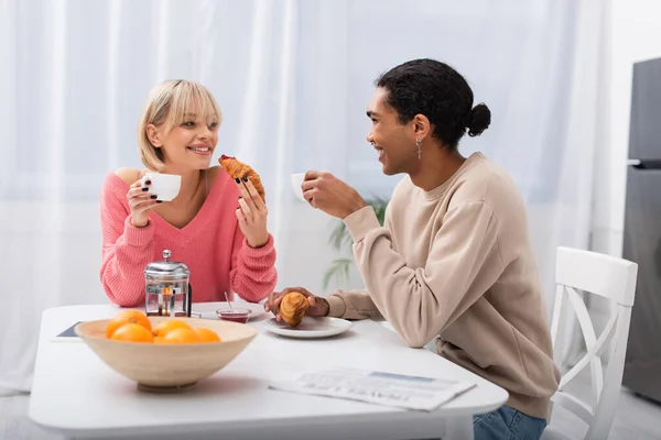 Happy multiethnic couple holding croissants during breakfast in morning — Stock Photo