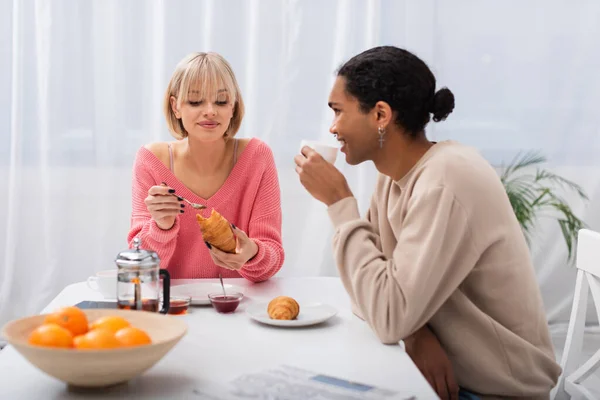 Happy african american man looking at girlfriend with croissant — Photo de stock