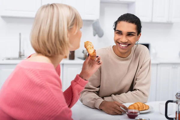 Allegro uomo africano americano guardando la ragazza bionda con croissant — Foto stock