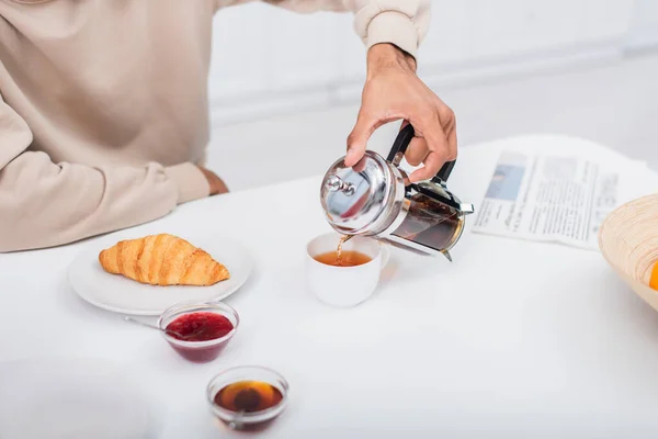 Vista recortada del hombre afroamericano vertiendo té en taza - foto de stock