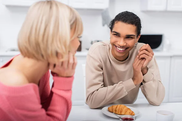 Smiling african american man looking at blurred blonde girlfriend in kitchen — Stock Photo