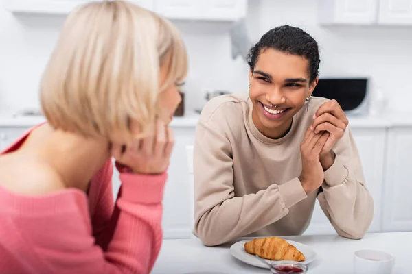 Lächelnder afrikanisch-amerikanischer Mann schaut verschwommene blonde Freundin in Küche an — Stockfoto